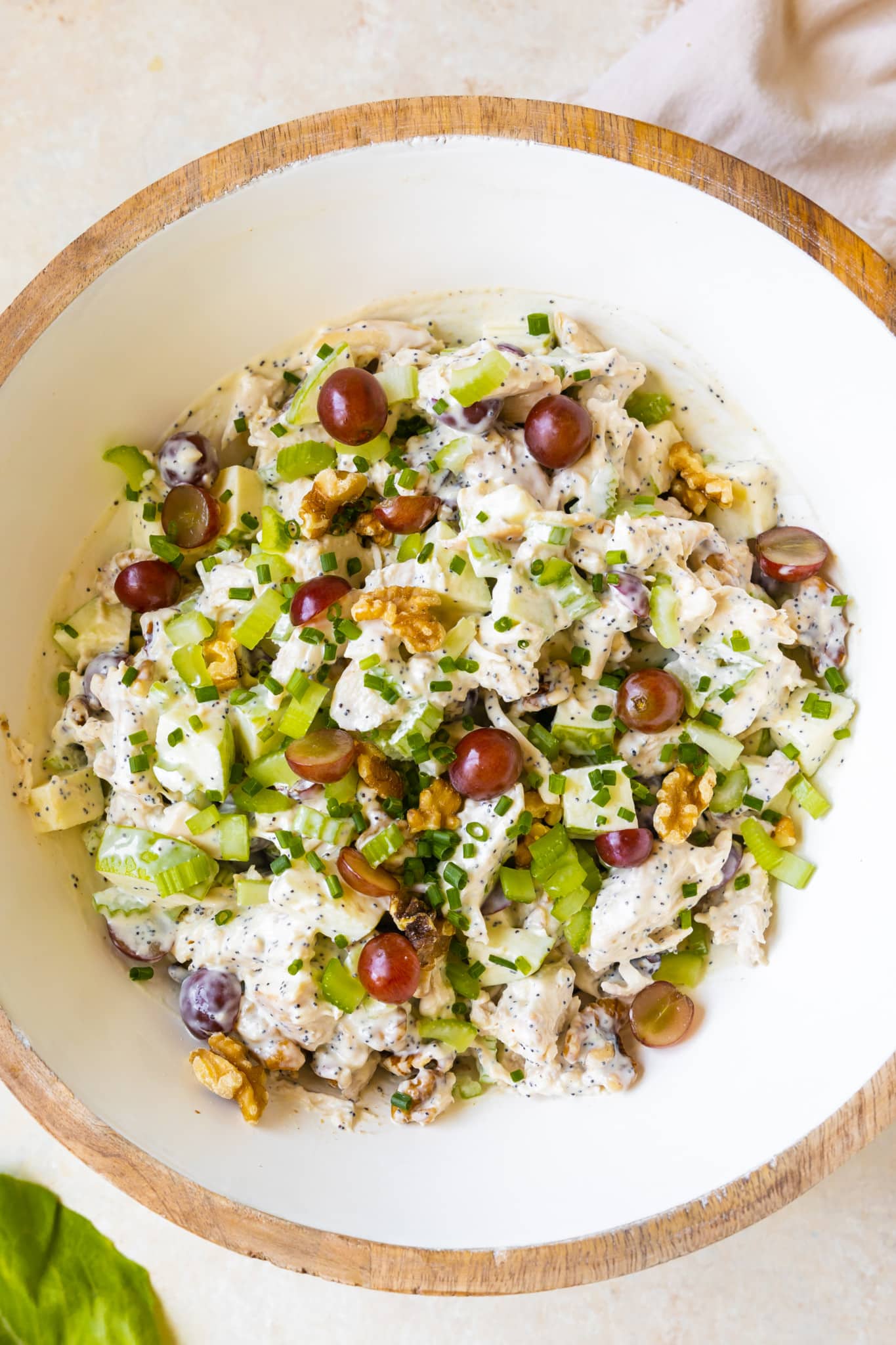 chicken salad garnished with chives, grapes and walnuts in a large white salad bowl. 