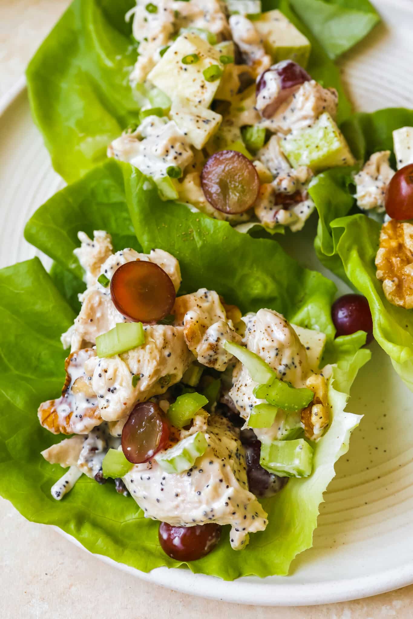 chicken salad with celery, grapes and walnuts in butter leaf lettuce wraps on a white plate. 