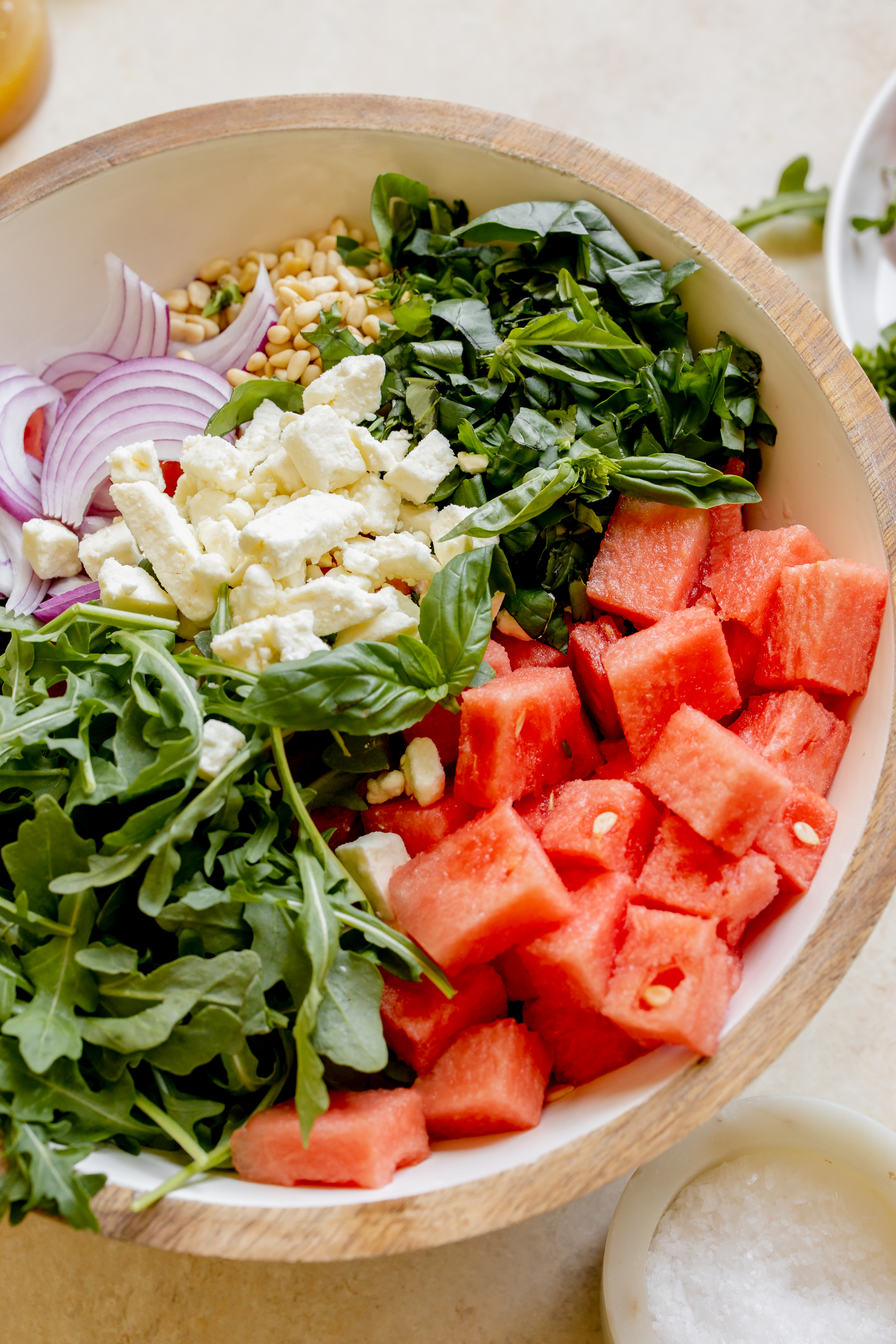 watermelon, arugula, basil, feta, pine nuts and red onion in a white salad bowl. 