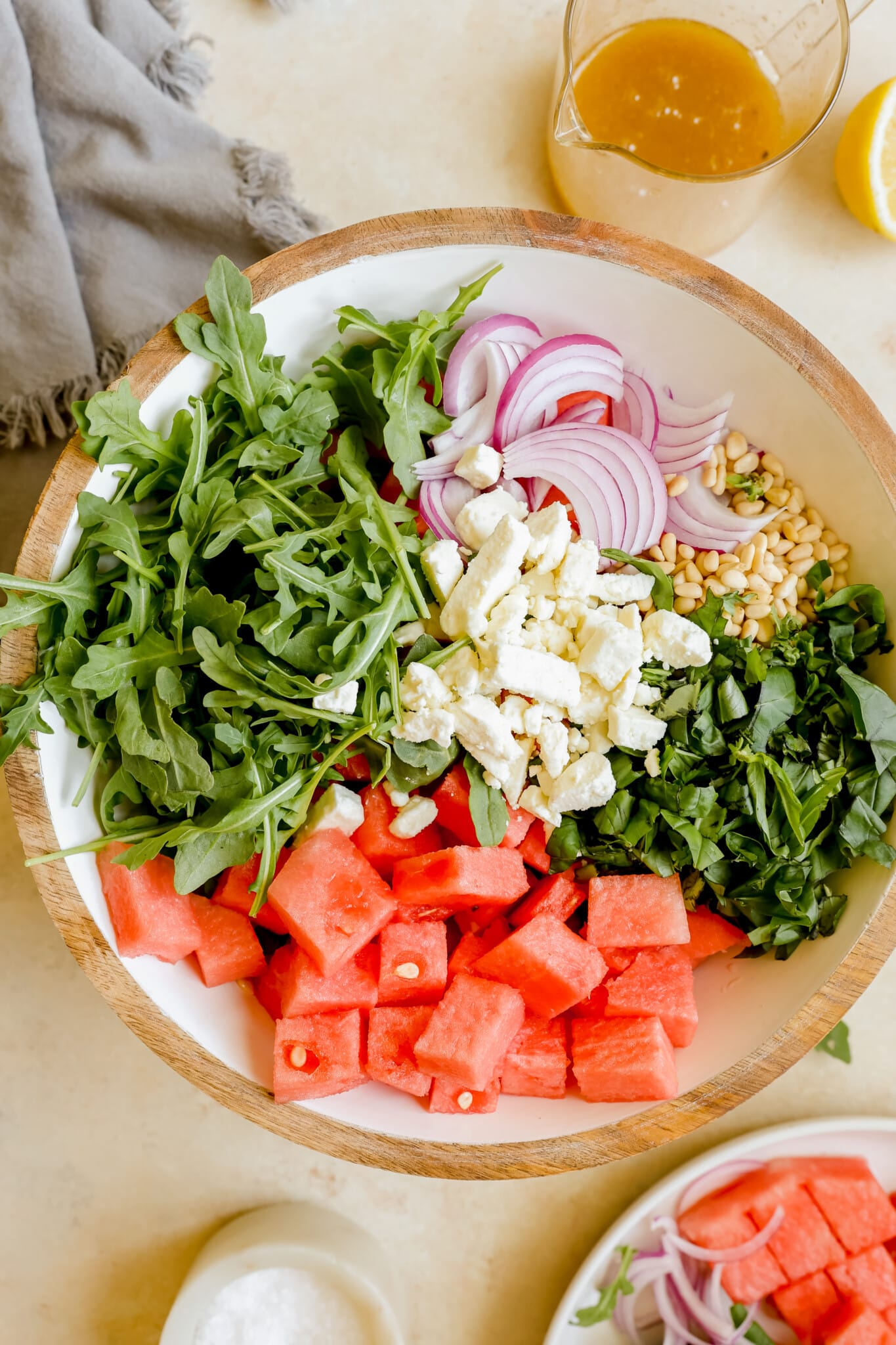 watermelon, arugula, basil, feta, pine nuts and red onion in a white salad bowl. 