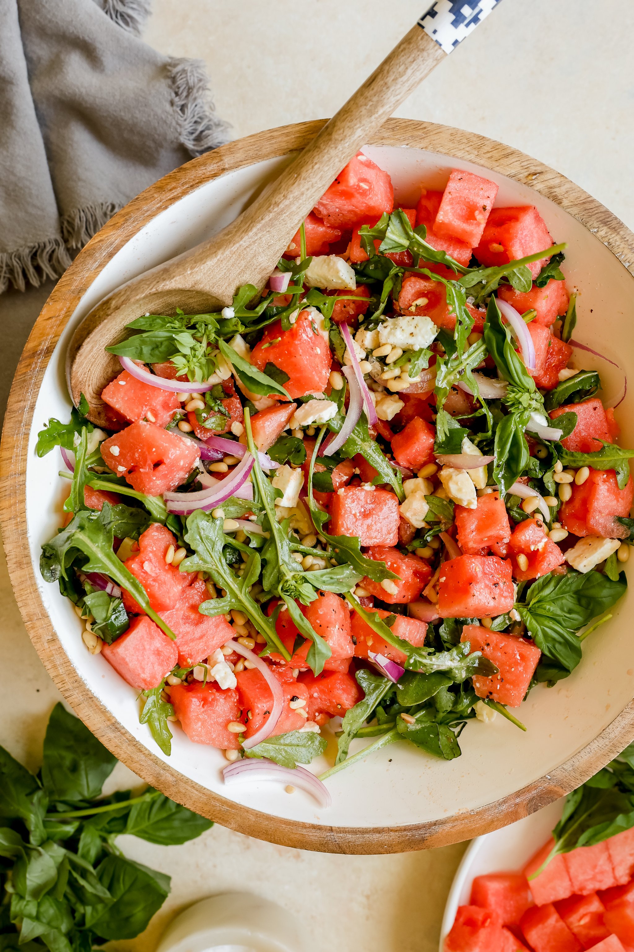 watermelon, arugula, basil, feta, pine nuts and red onion in a white salad bowl. 