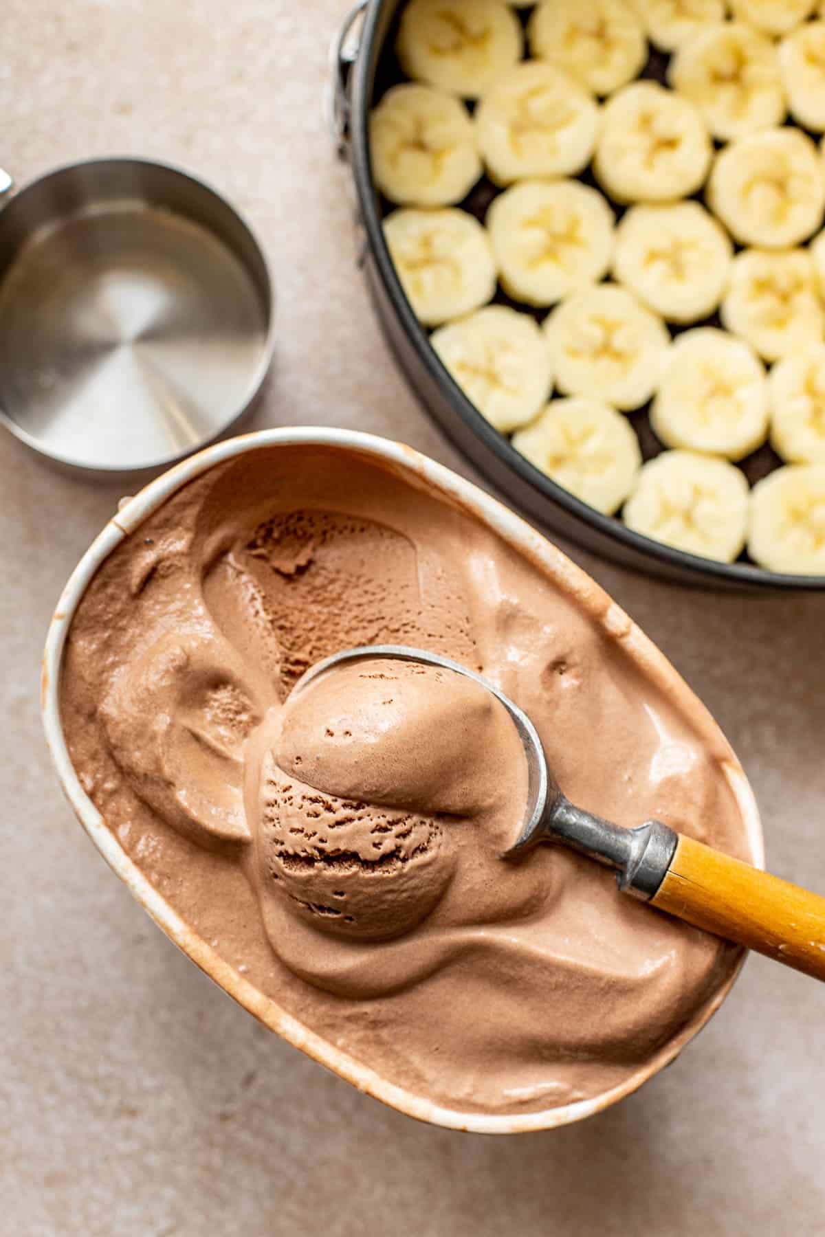 an ice cream scoop scooping out softened chocolate ice cream from the container. 