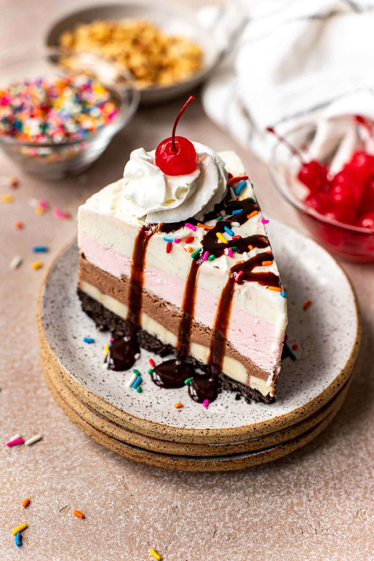 a slice of ice cream pie on a stack of speckled plates with chocolate syrup on top. 