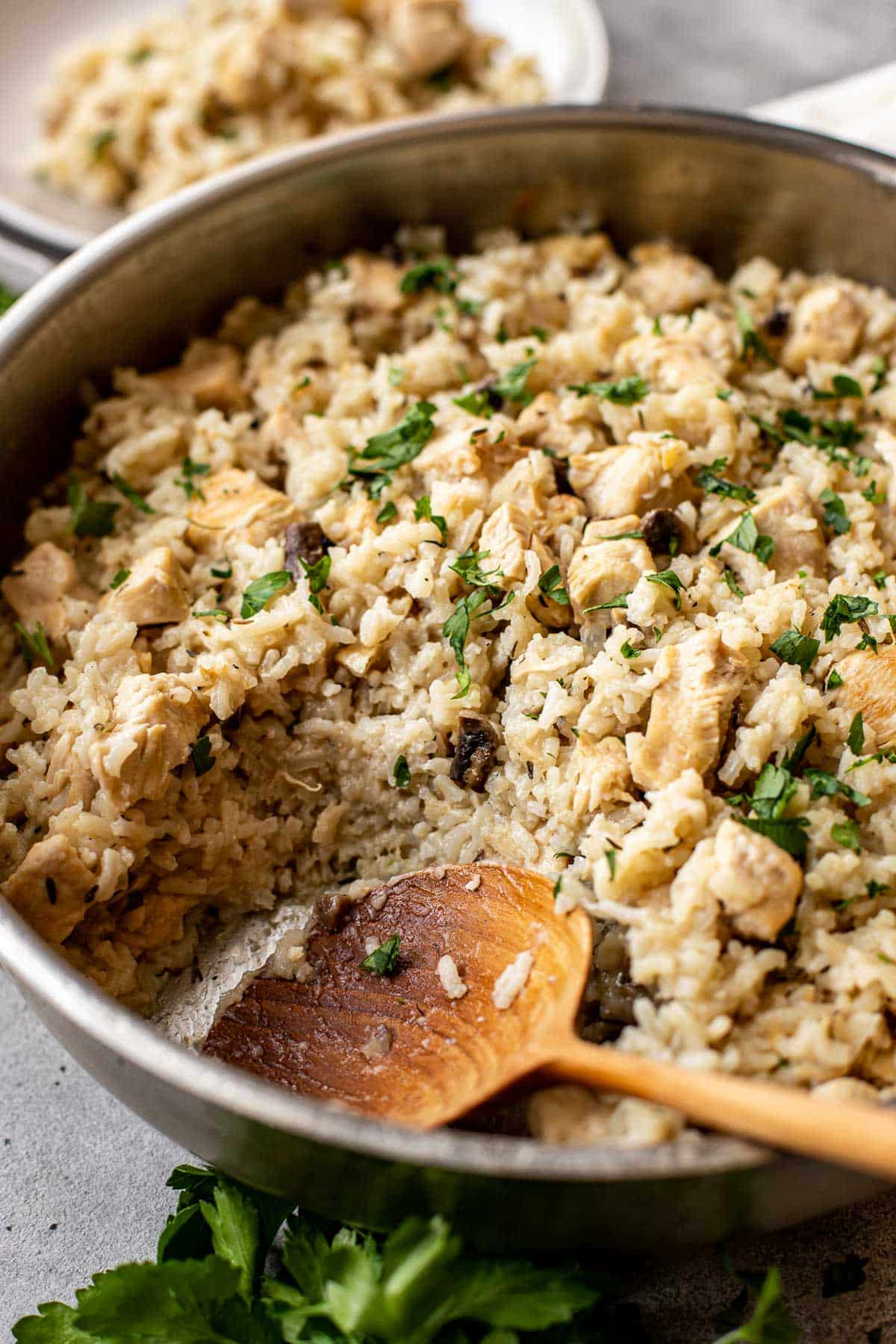 Chicken and rice topped with parsley in a sauté pan with a wooden spoon. 