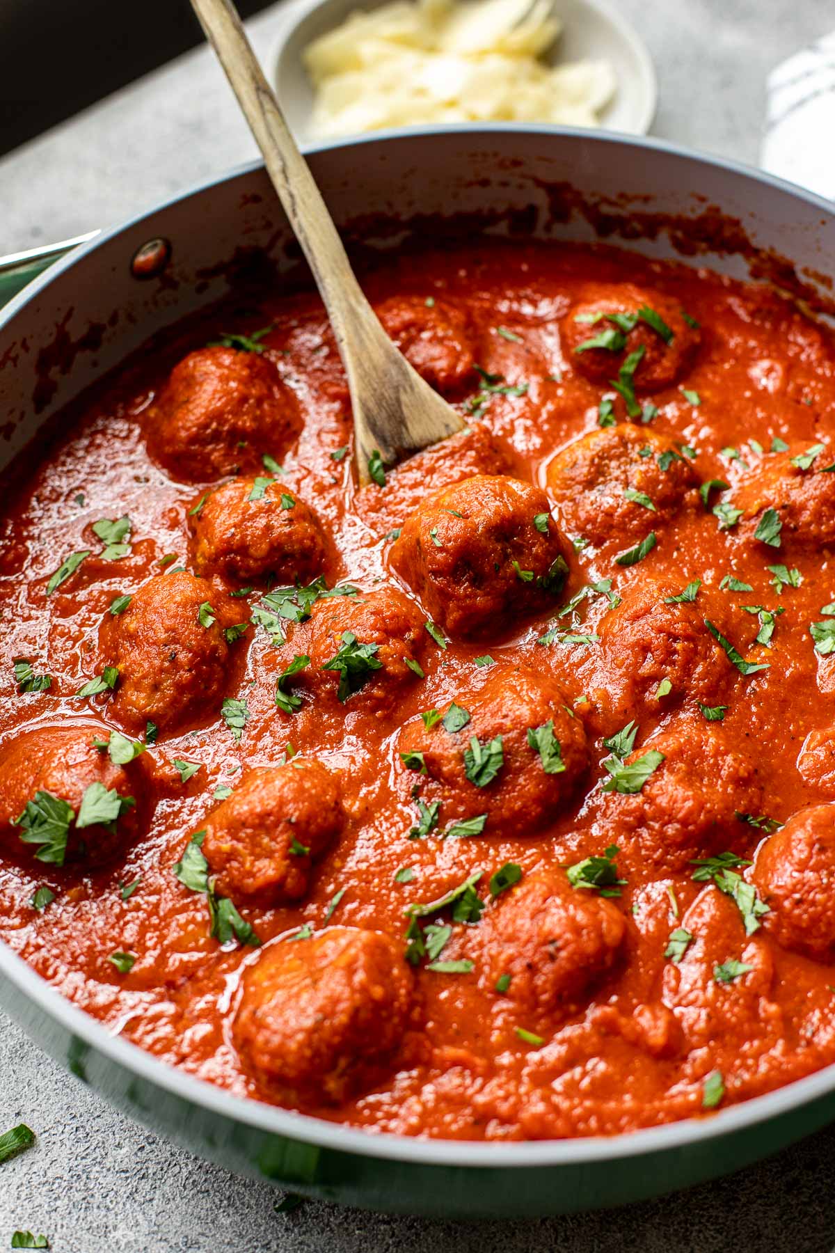 Meatballs in a pan covered in red sauce and garnished with parsley. 