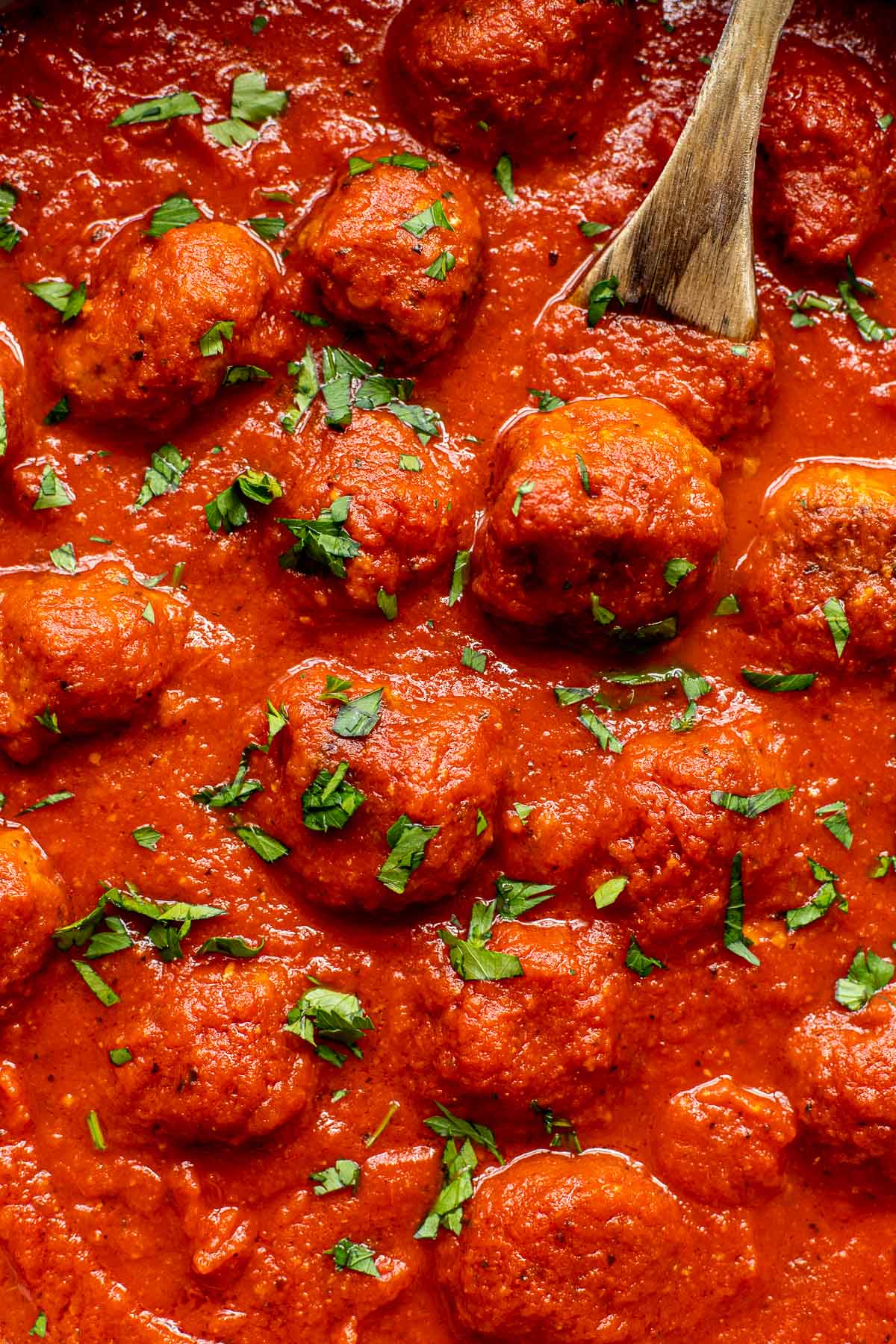 An up close image of beef meatballs in red sauce garnished with parsley. 
