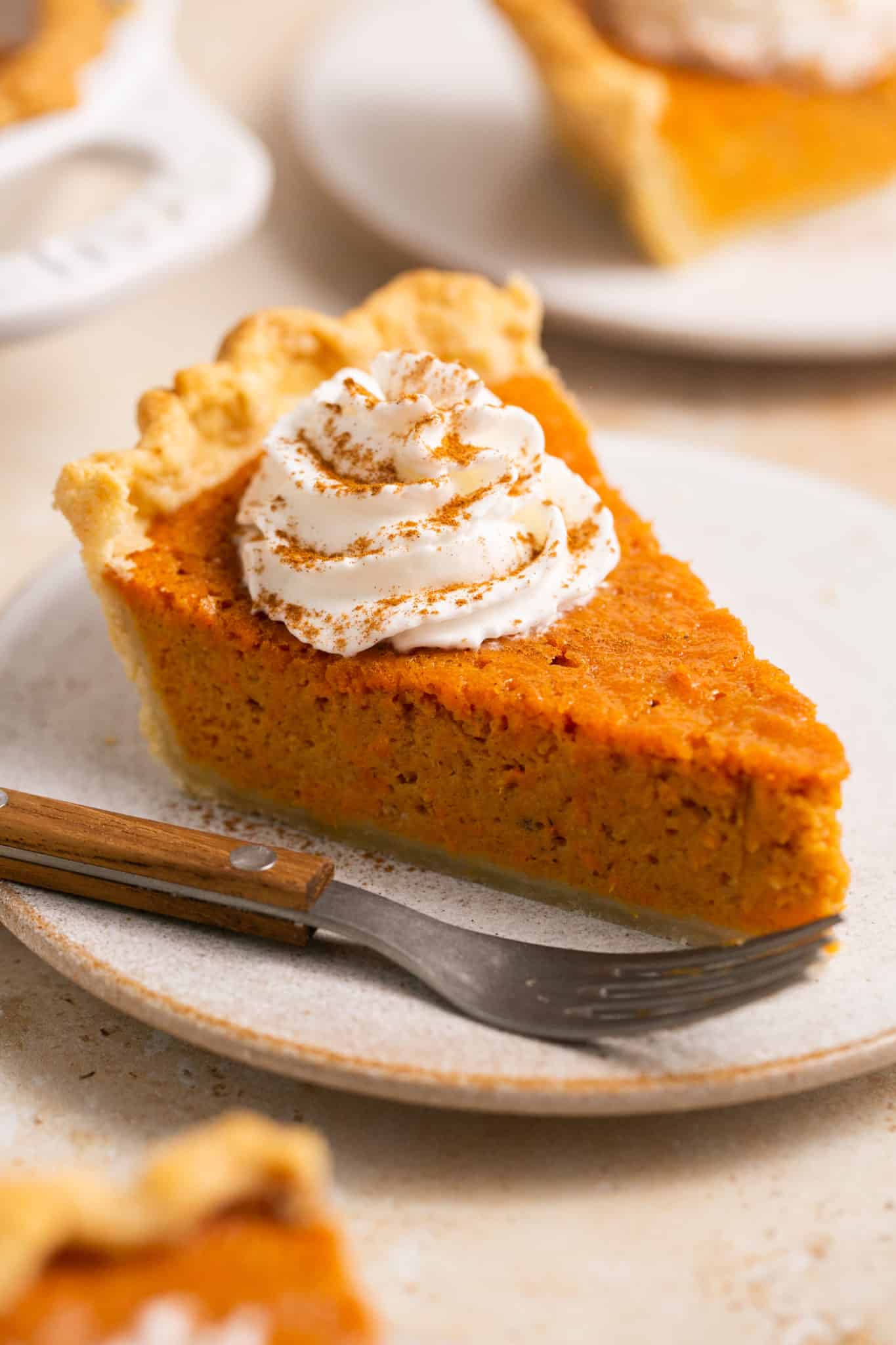 A slice of sweet potato pie on a white plate topped with whipped cream. 
