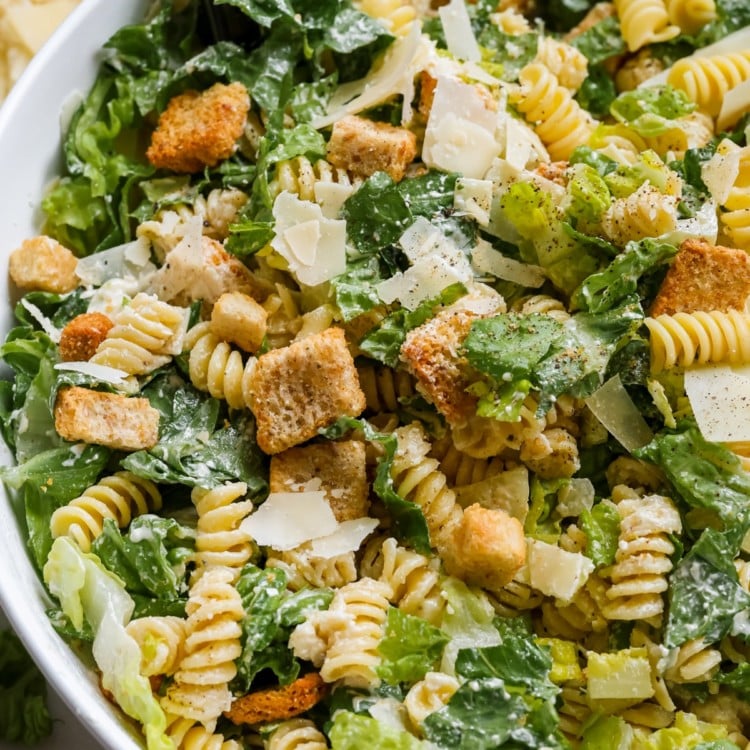 white bowl with a salad made of romaine lettuce, rotini pasta, croutons, parmesan cheese, salt and pepper