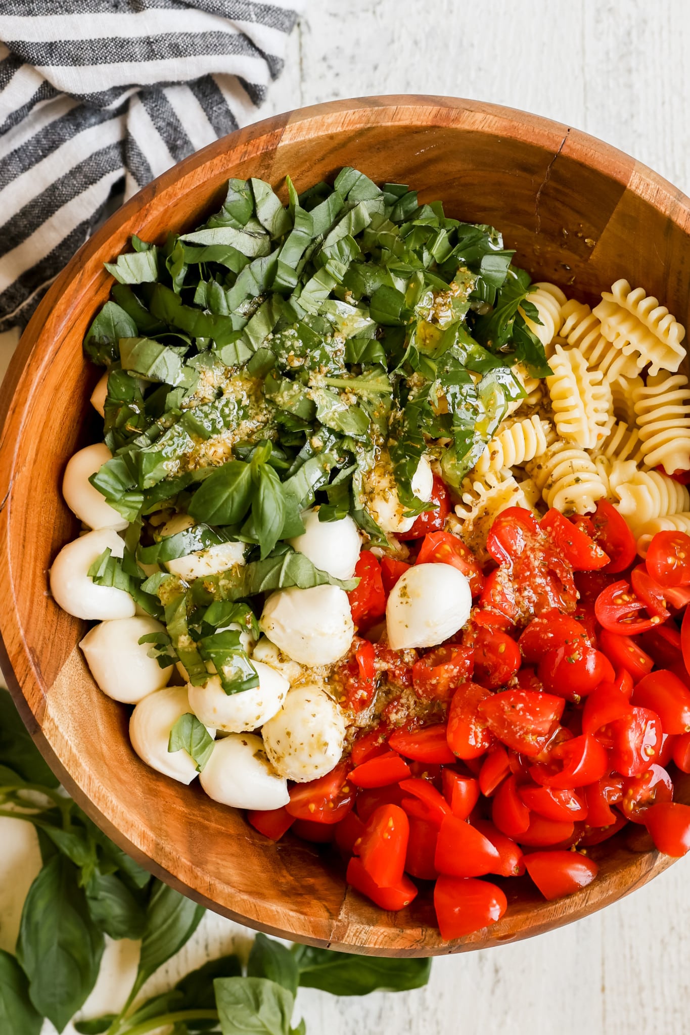 pasta, basil, mozzarella and tomatoes in a wooden salad bowl with dressing on top. 