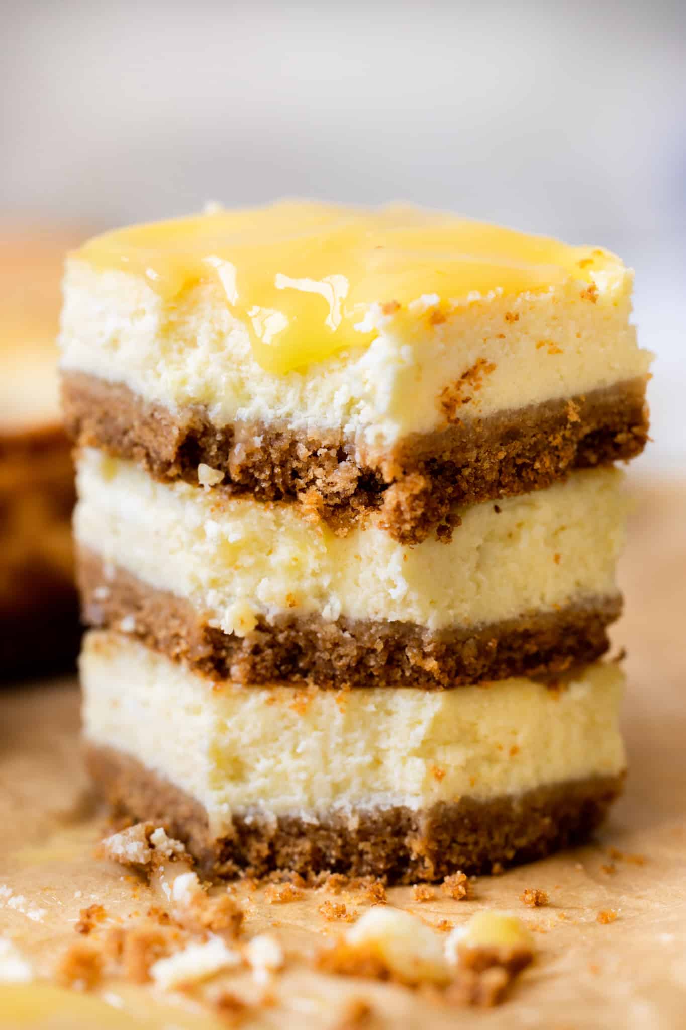 lemon cheesecake bars stacked on top of each other with lemon curd on top. 