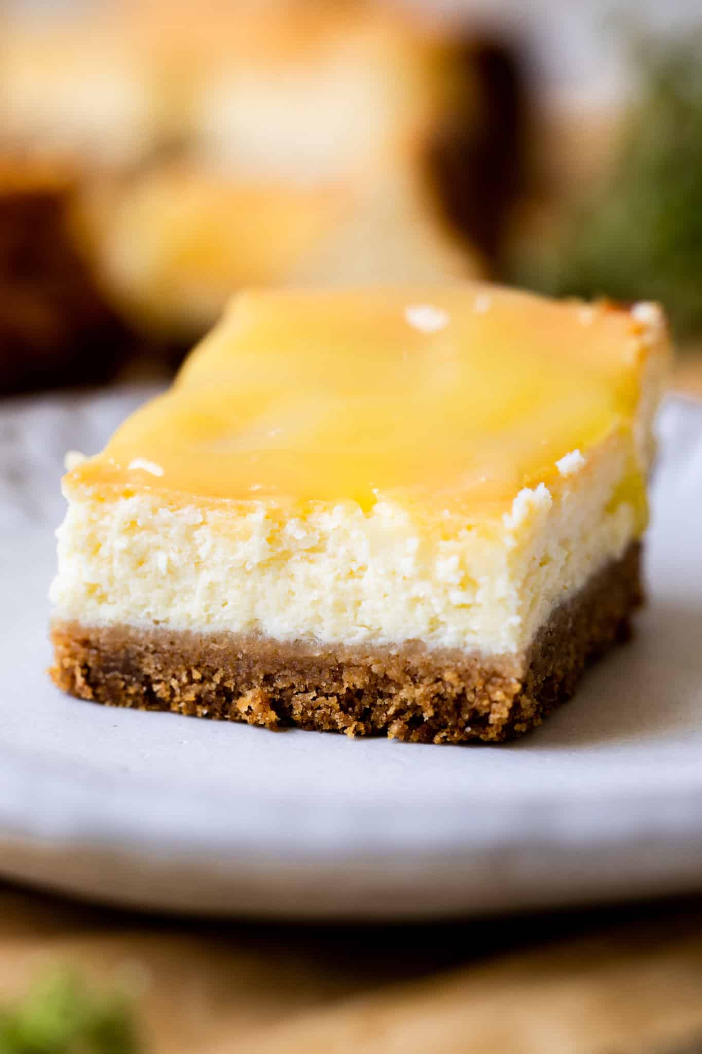 a lemon cheesecake bar on a white plate topped with lemon curd. 