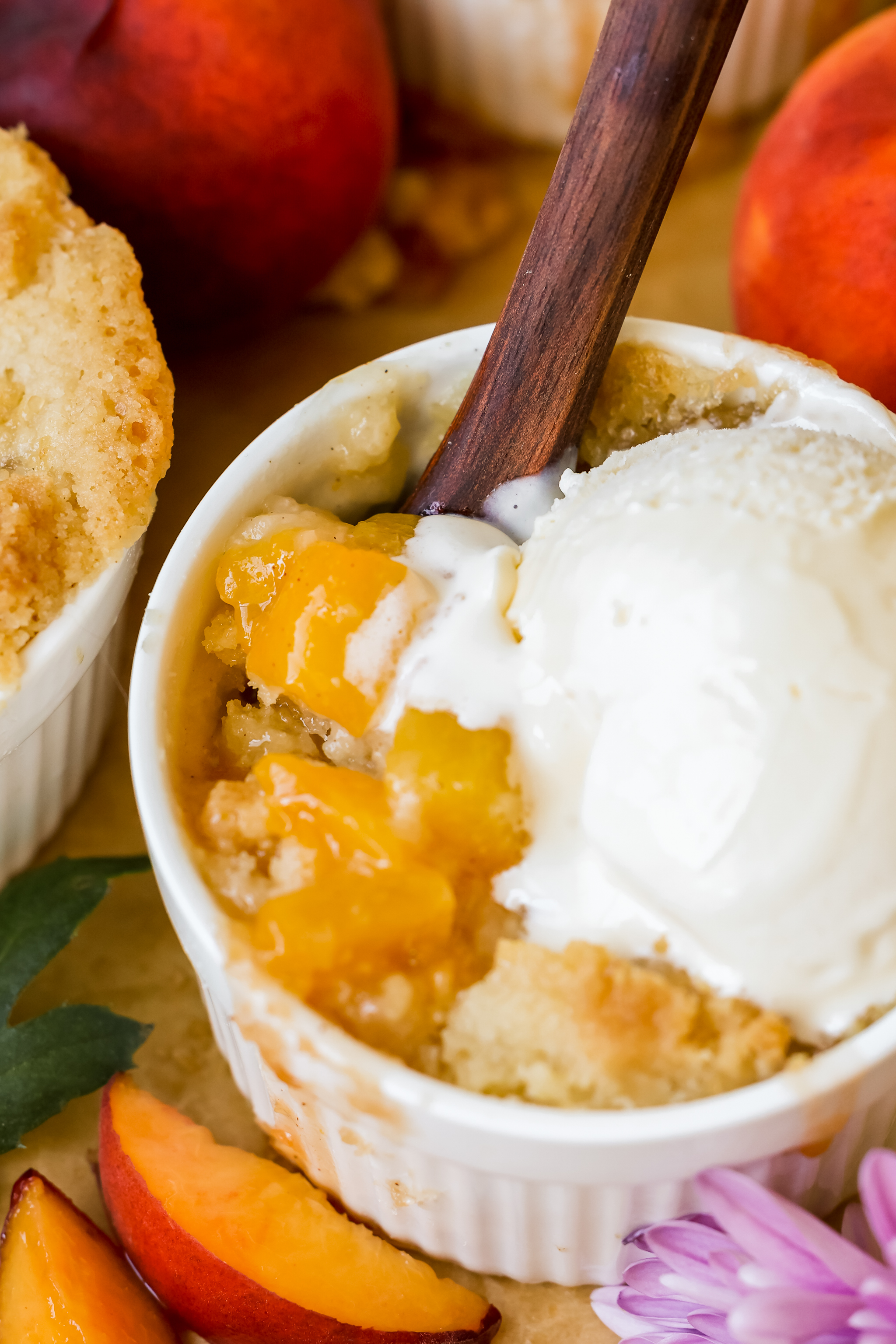 a spoon digging into a peach cobbler with ice cream on top. 