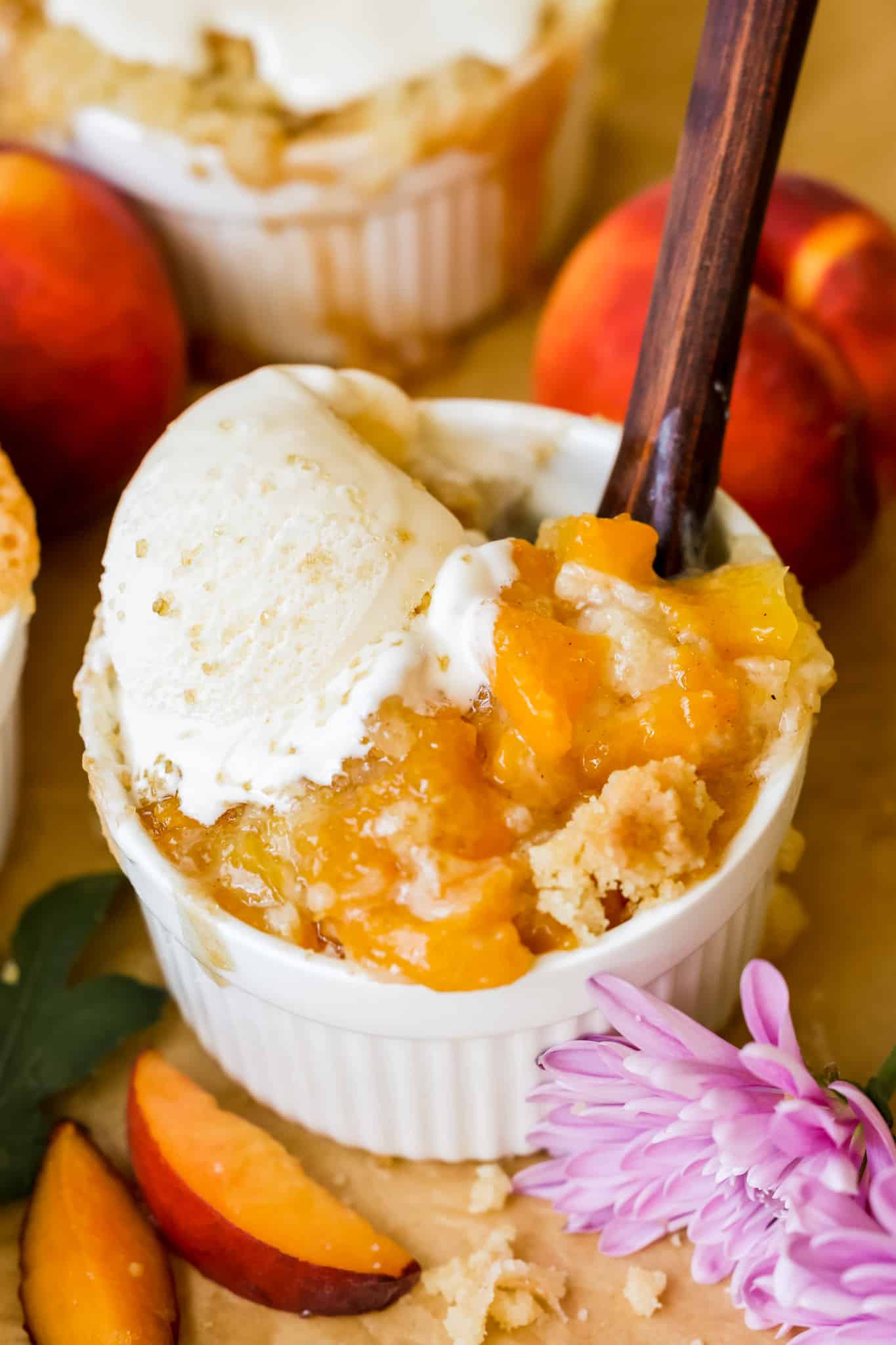 a spoon digging into a peach cobbler with ice cream on top. 