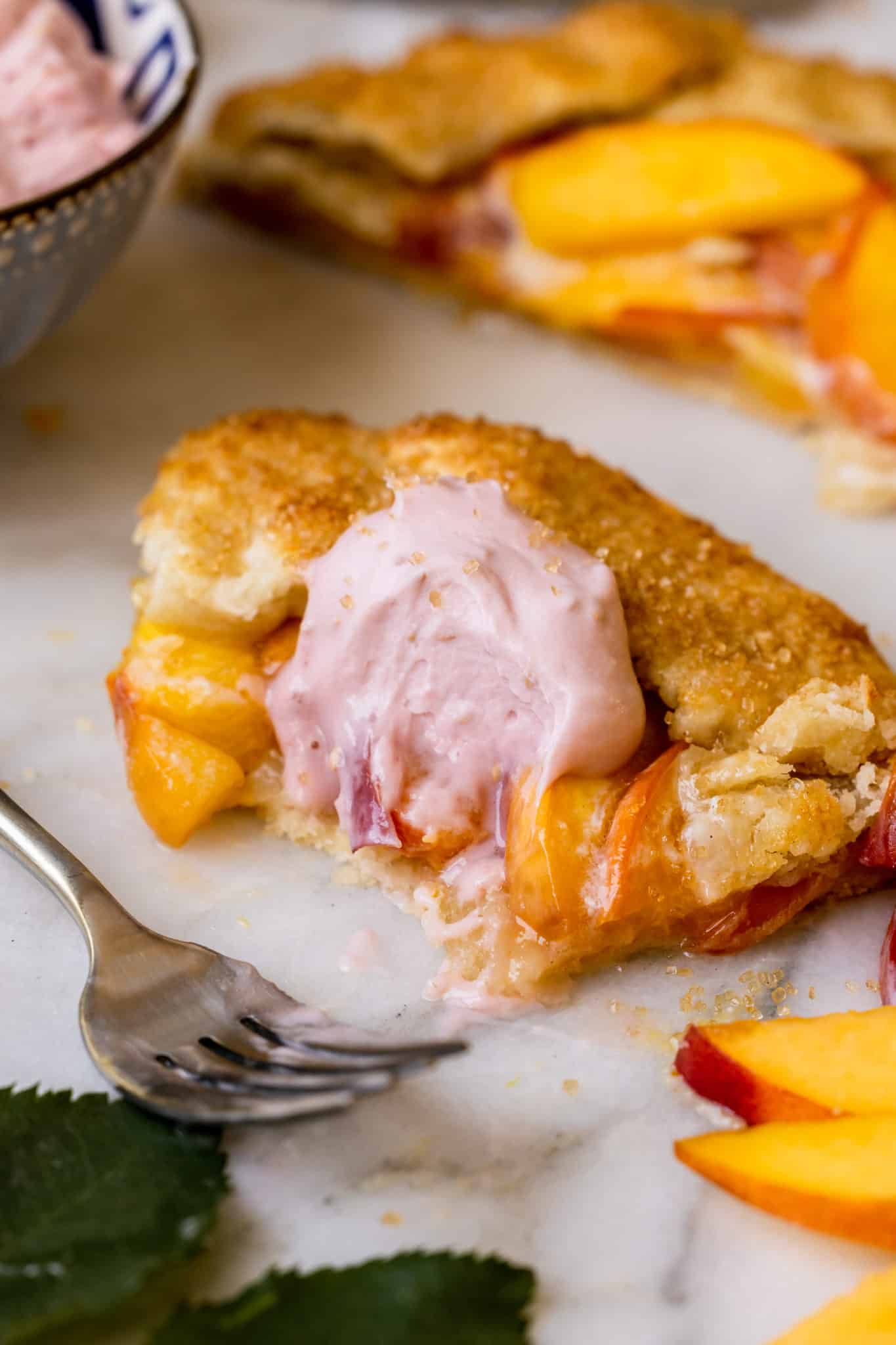 a bite taken out of a galette made with peaches and topped with raspberry whipped cream. 