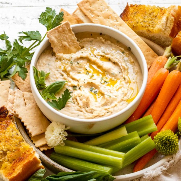 A plate of hummus, vegetables, and crackers.