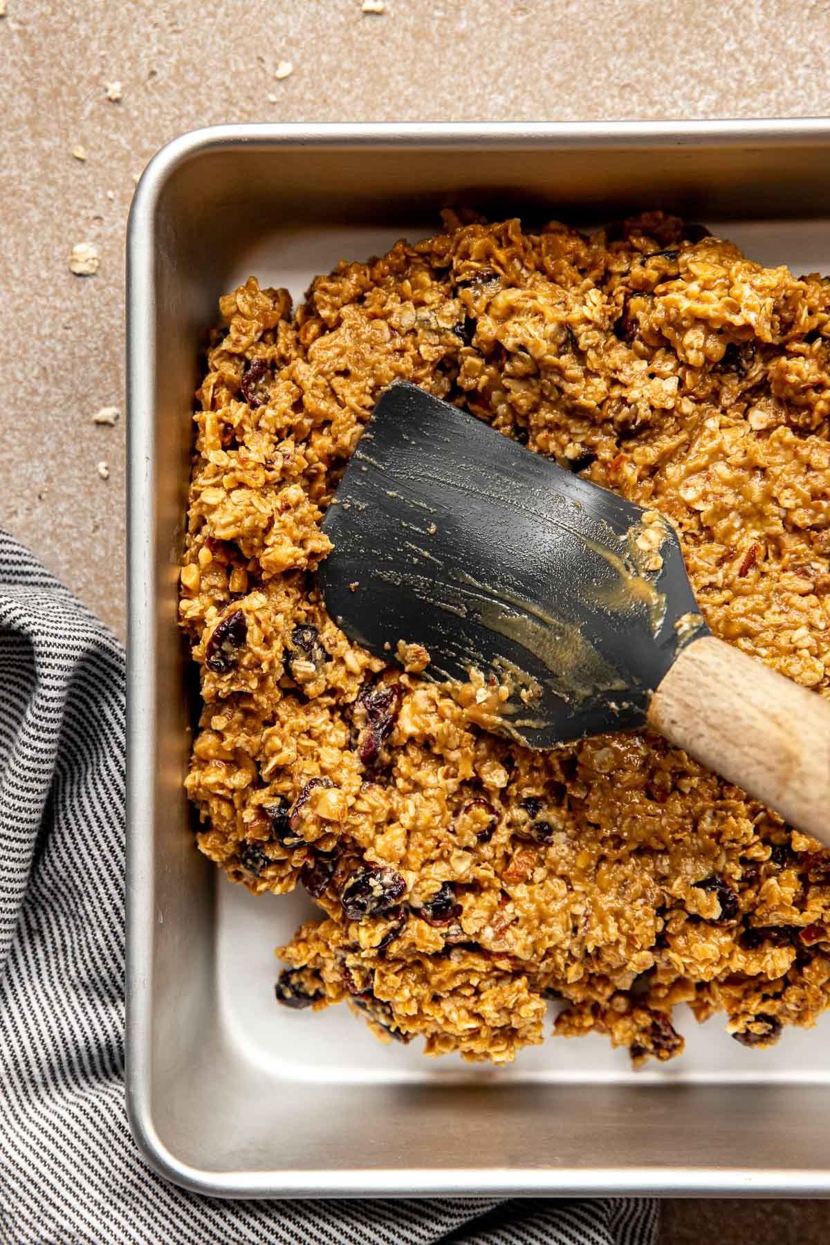 a black rubber spatula pressing down energy bar mixture into a pan. 