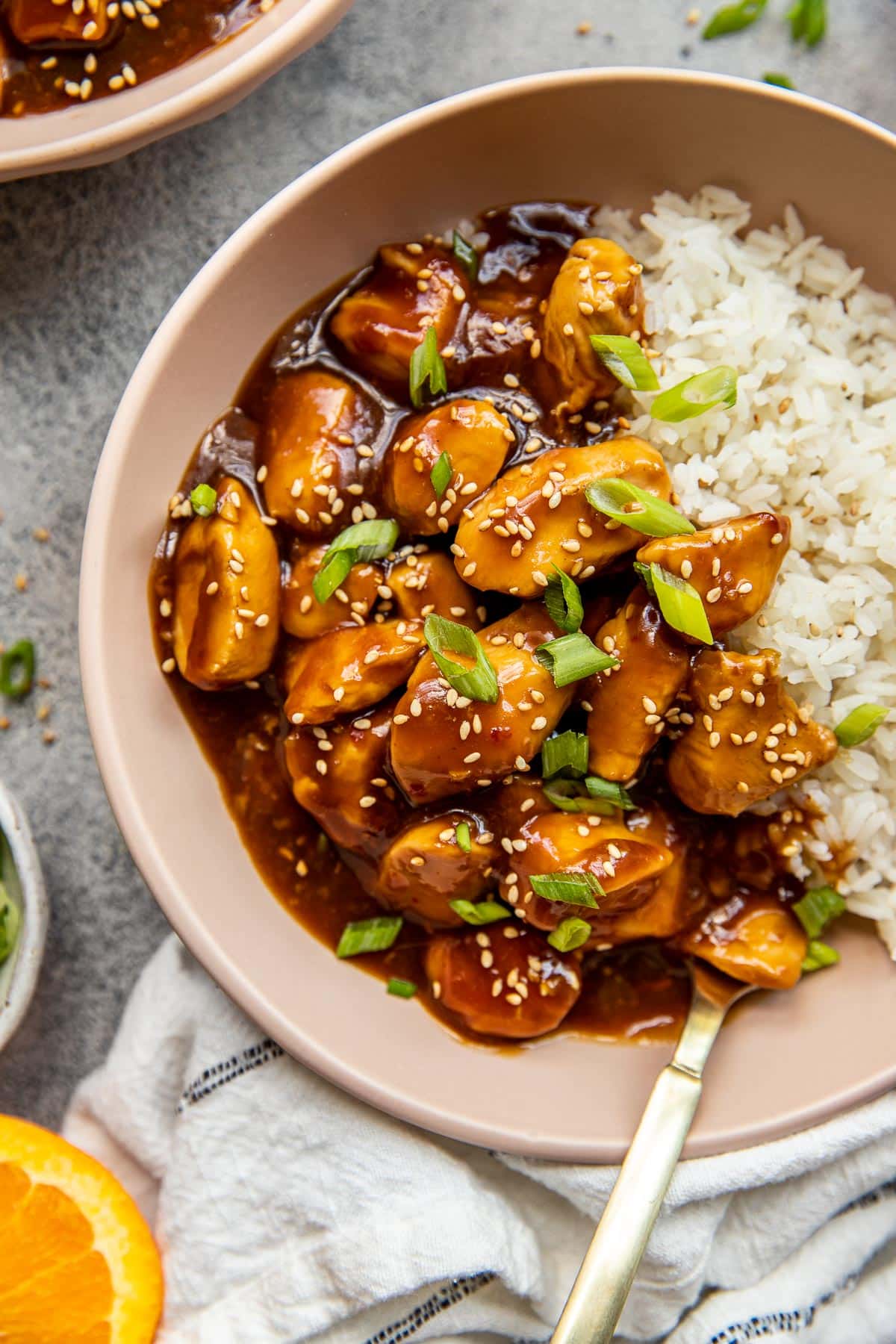 orange chicken with rice in a bowl garnished with green onions and sesame seeds. 