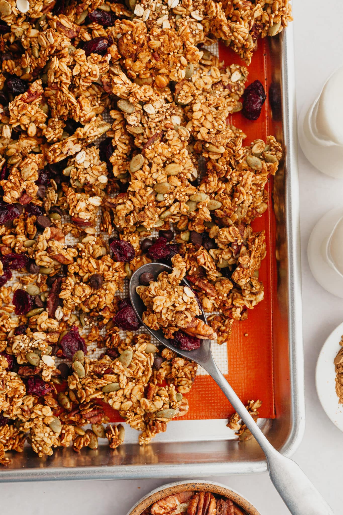 granola on a baking sheet with a spoon. 