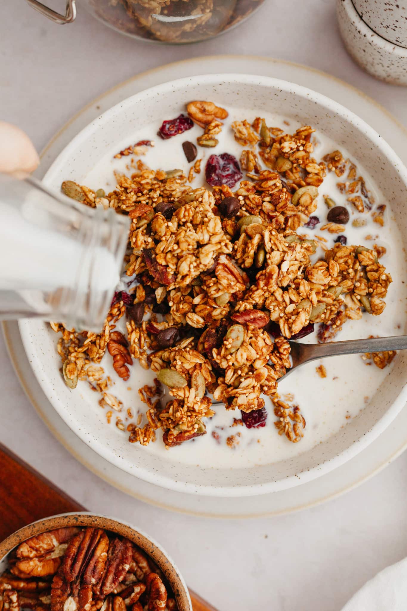 milk being poured onto granola in a white speckled bowl. 