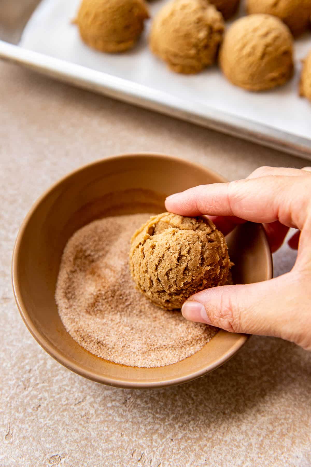 a womans hand rolling cookie dough in cinnamon and sugar. 