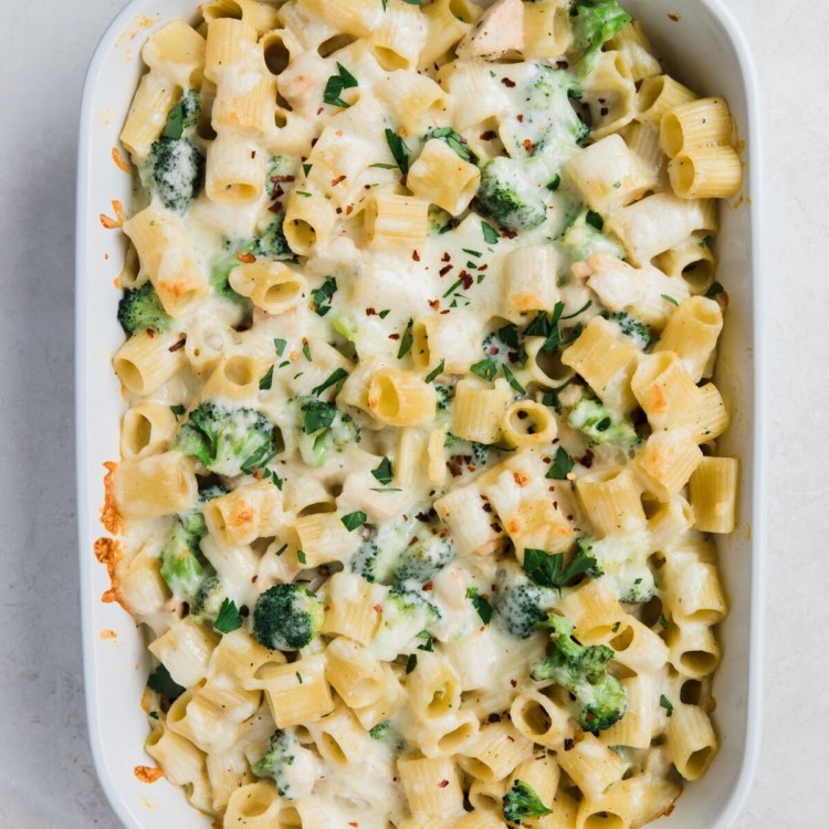 white casserole dish full of noodles, white sauce, cheese, and spinach