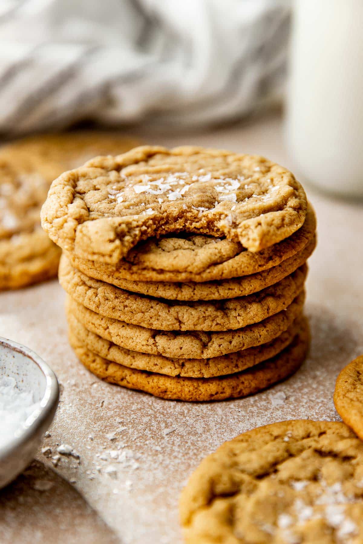 a stack of cookies with a bite taken out of the cookie on top garnished with flaky sea salt. 