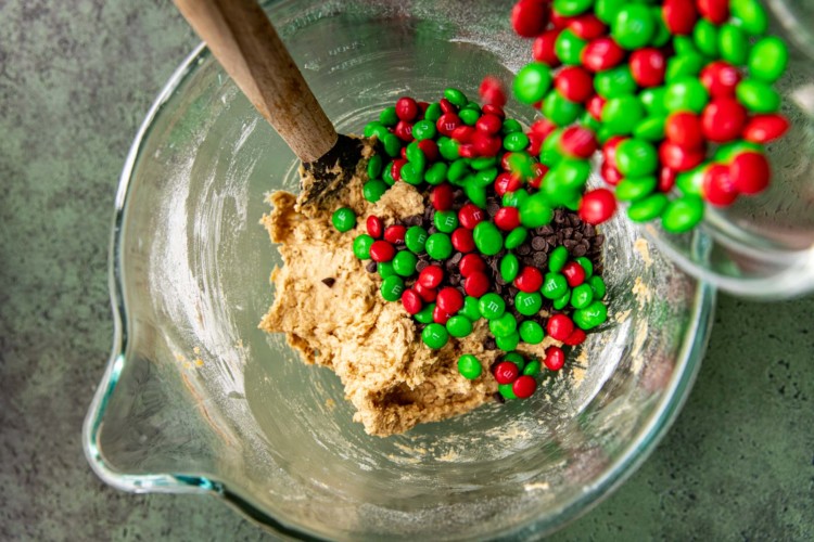 pouring red & green m&ms into cookie dough mixture