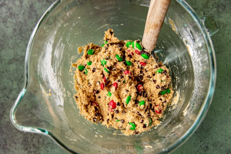 red and green m&ms mixed in cookie dough in a clear bowl