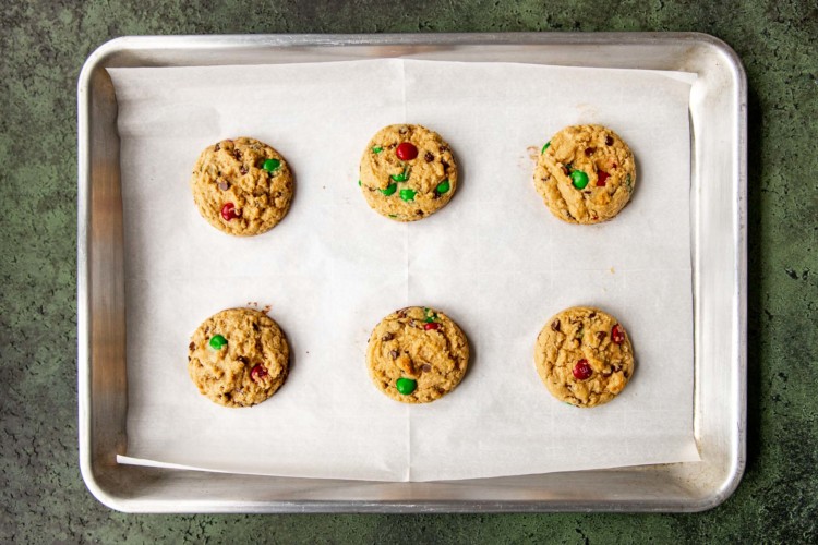 six partially baked cookies with red and green m&ms on a baking sheet