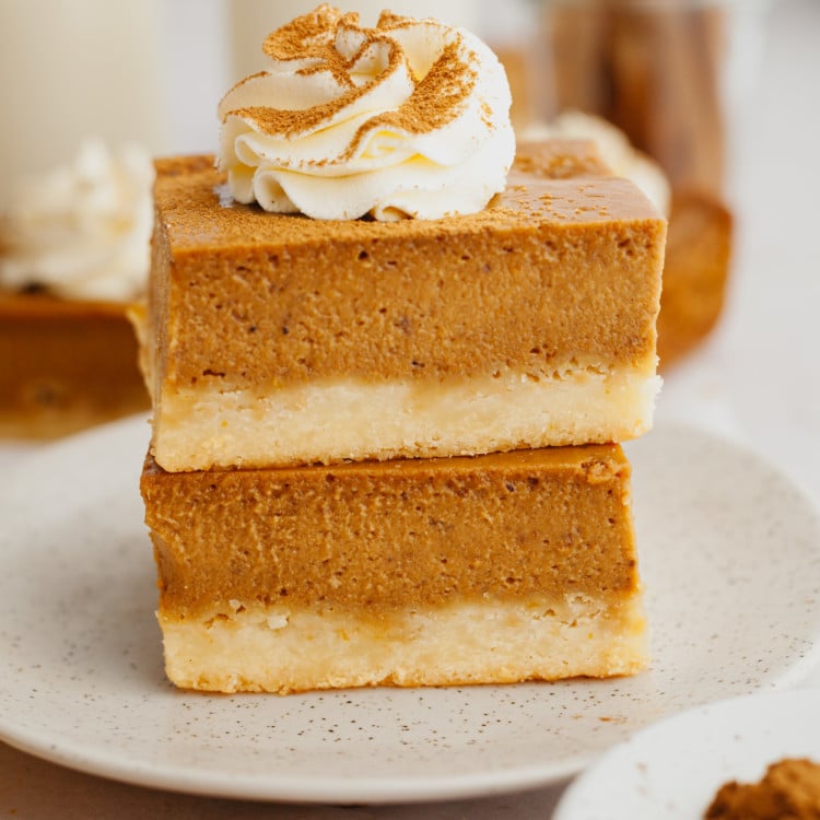 two pumpkin pie bars stacked on a tan plate and topped with a whipped cream swirl