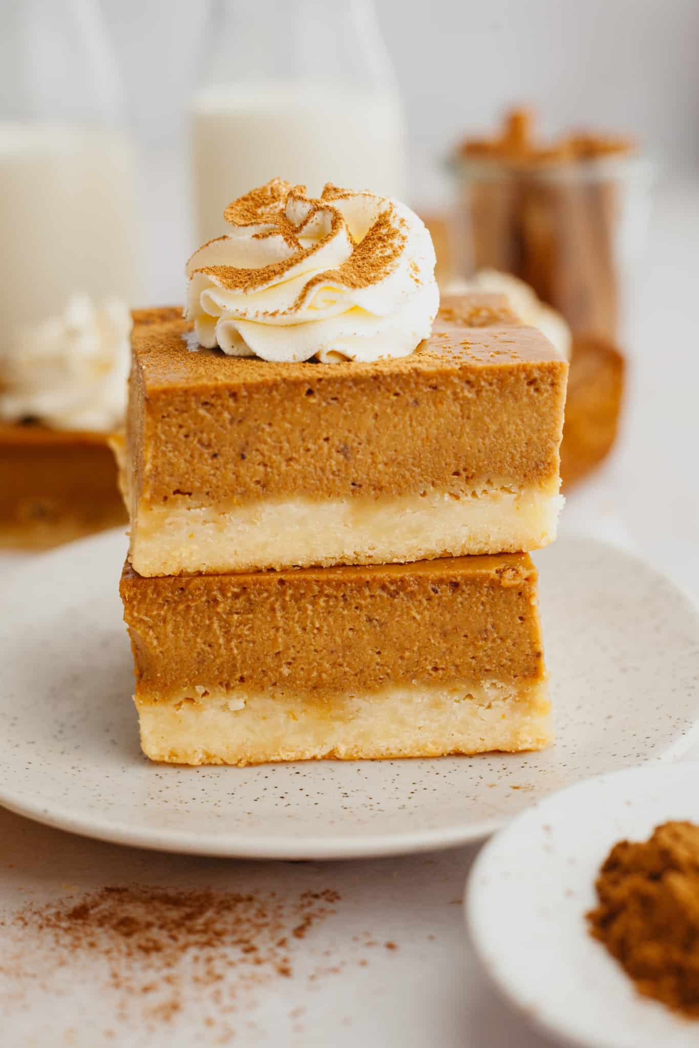 two pumpkin pie bars stacked on a tan plate and topped with a whipped cream swirl