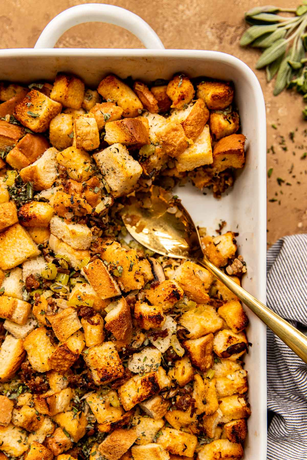 stuffing in a white casserole dish with a gold serving spoon. 