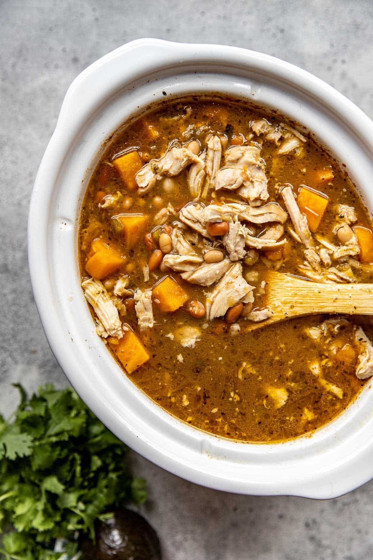 chicken chili in a white slow cooker with shredded chicken and sweet potatoes. 