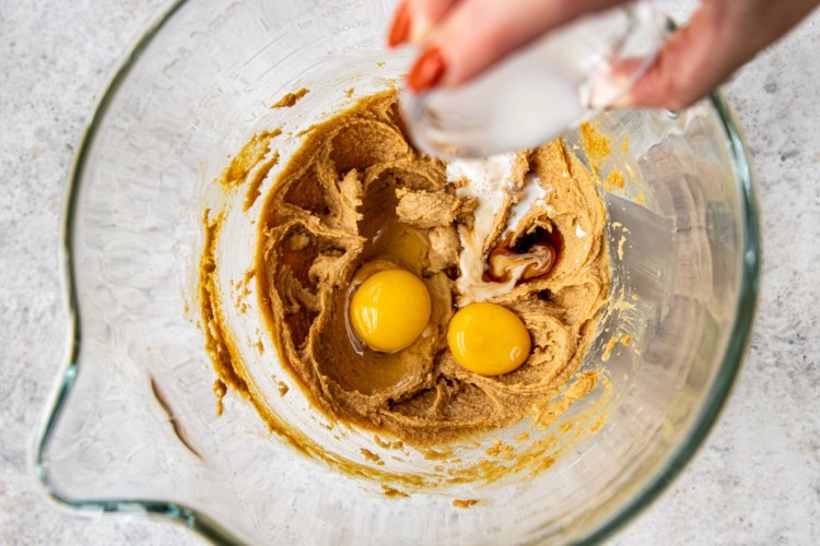 woman's hand pouring ingredients into bowl with cookie batter