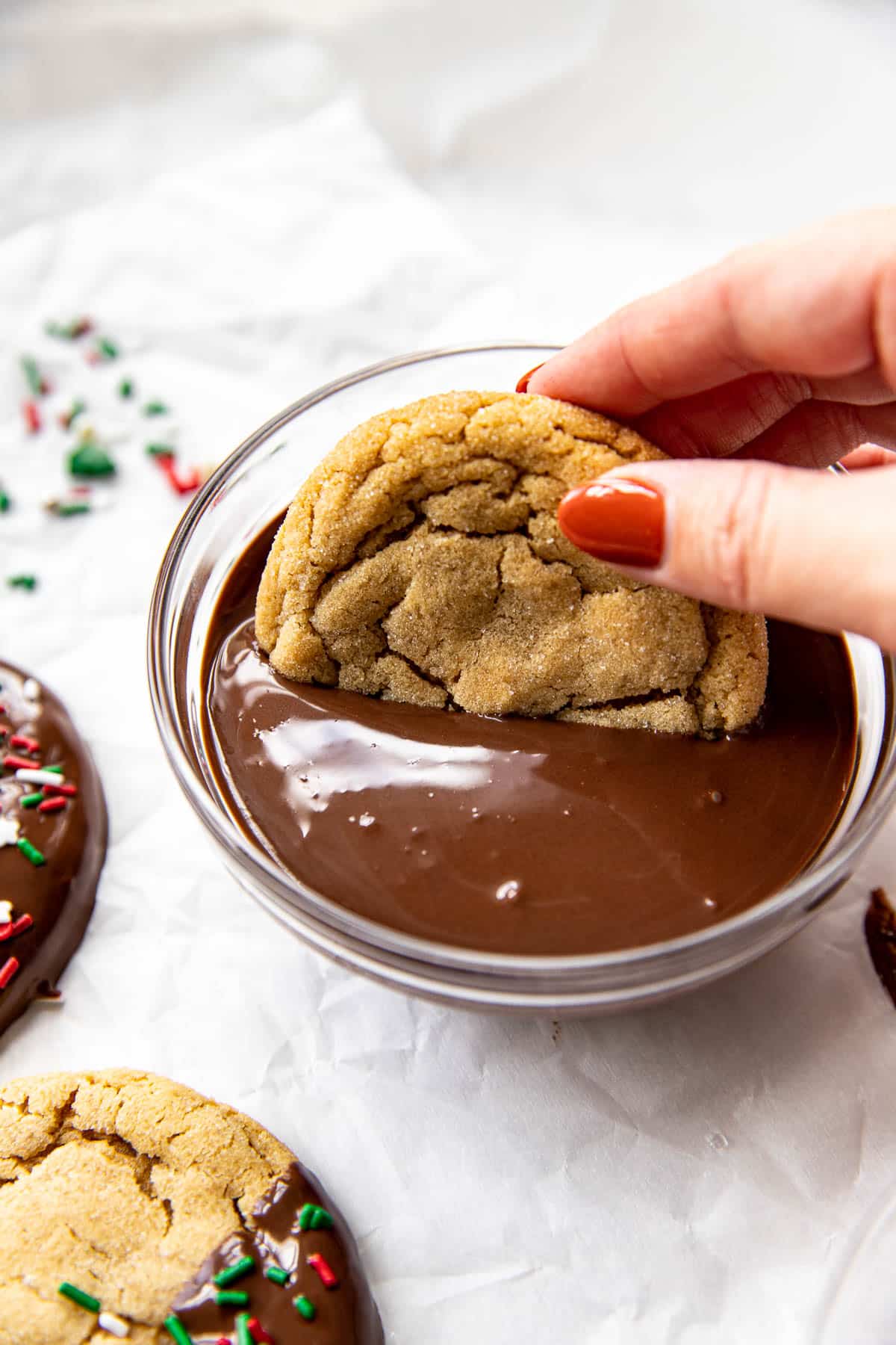 a hand dipping a peanut butter cookie into melted dark chocolate. 