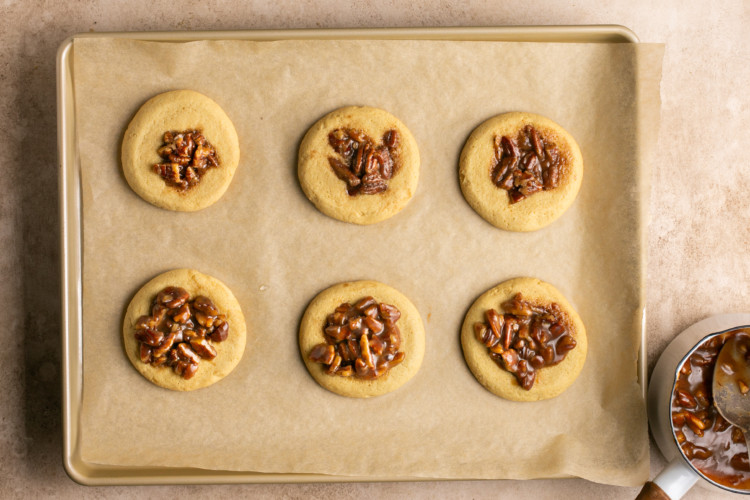 six cookies on a baking sheet topped with pecans