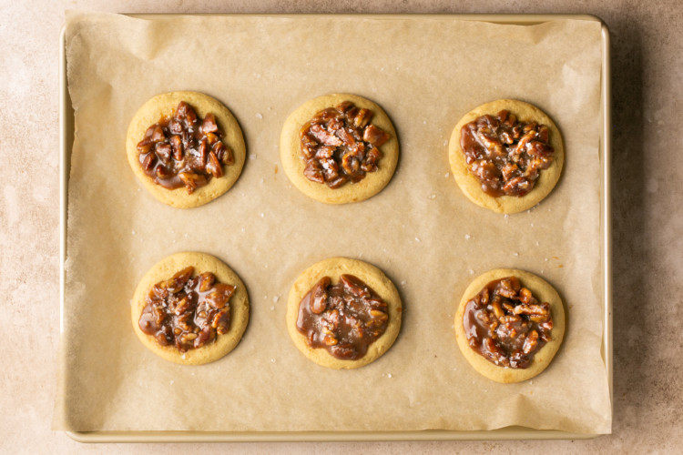 six cookies on a baking sheet topped with pecans