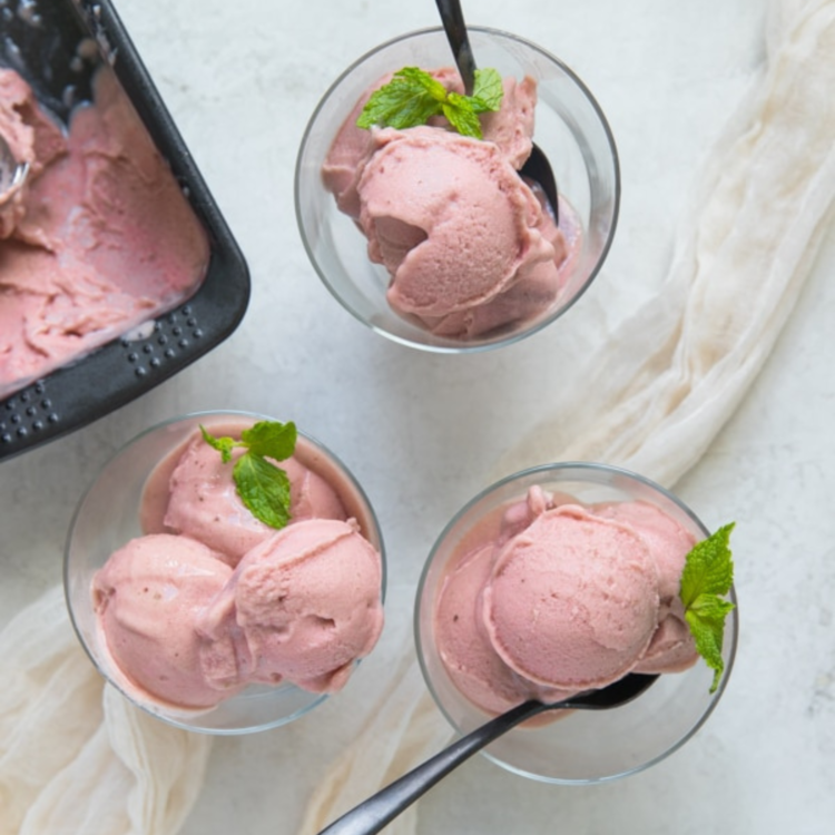 three clear bowls with pink ice cream, green herbs, and spoons