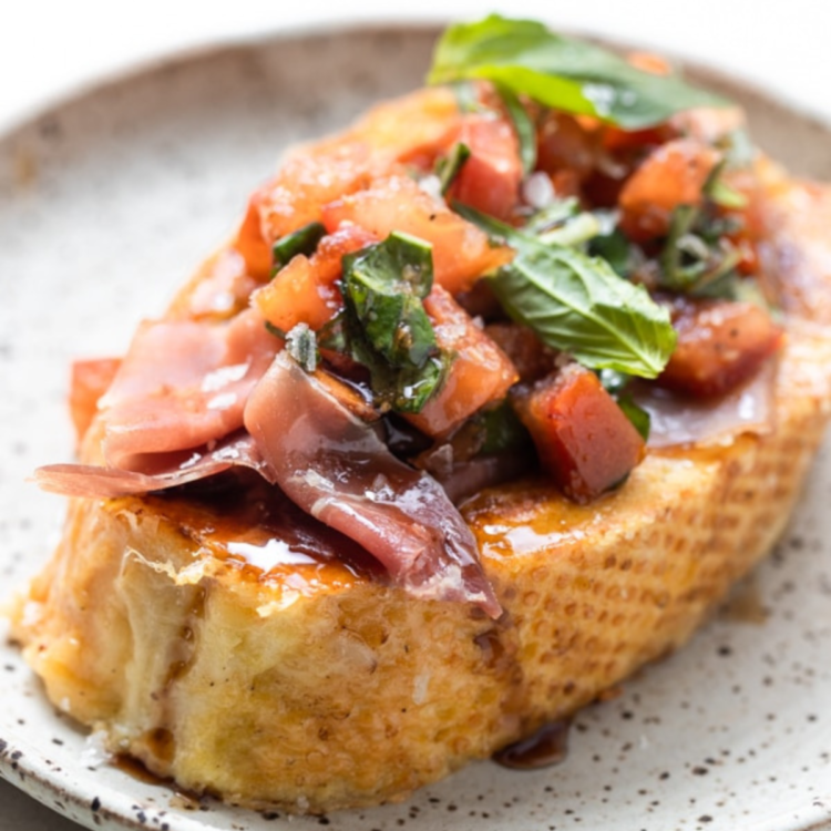 piece of toast topped with tomatoes, greens, prosciutto