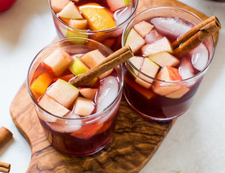 three glasses with sangria, sliced fruit, and cinnamon sticks on a platter