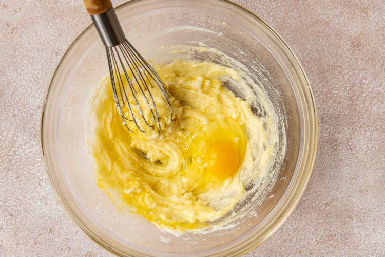 clear bowl with an egg being whisked into a butter and sugar mixture