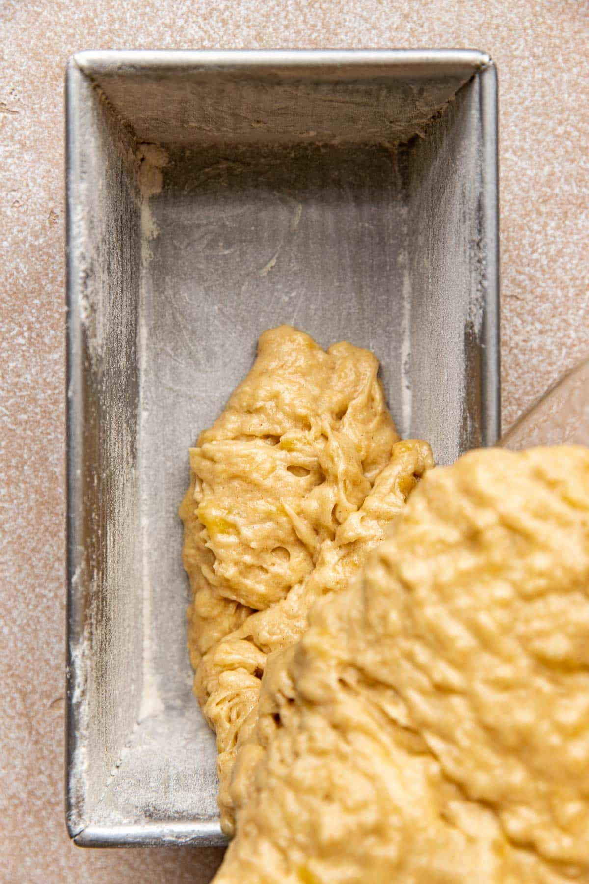 banana bread batter being poured into a greased and floured