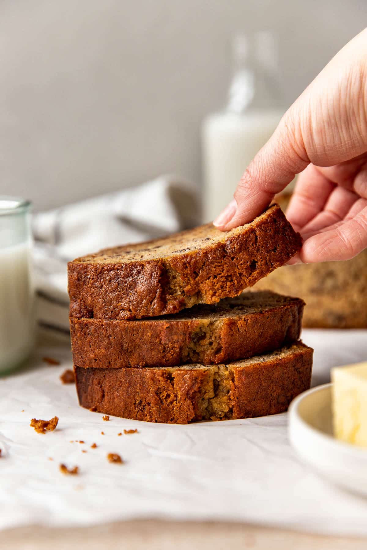 a womans hand lifting up a slice of banana bread. 