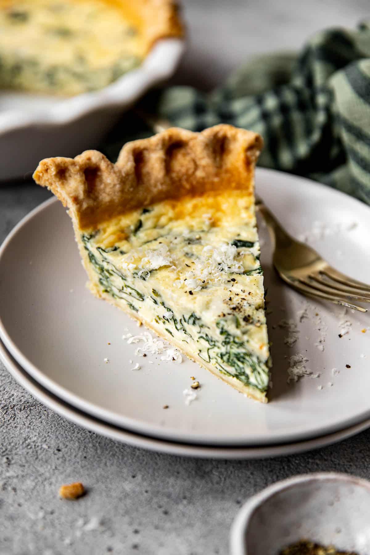 A slice of quiche florentine on a plate with Parmesan on top. 