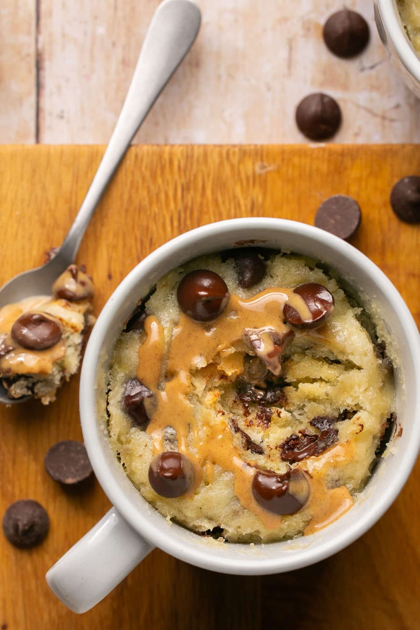 a spoon that has taken a bite out of a mug cake topped with chocolate chips and peanut butter. 