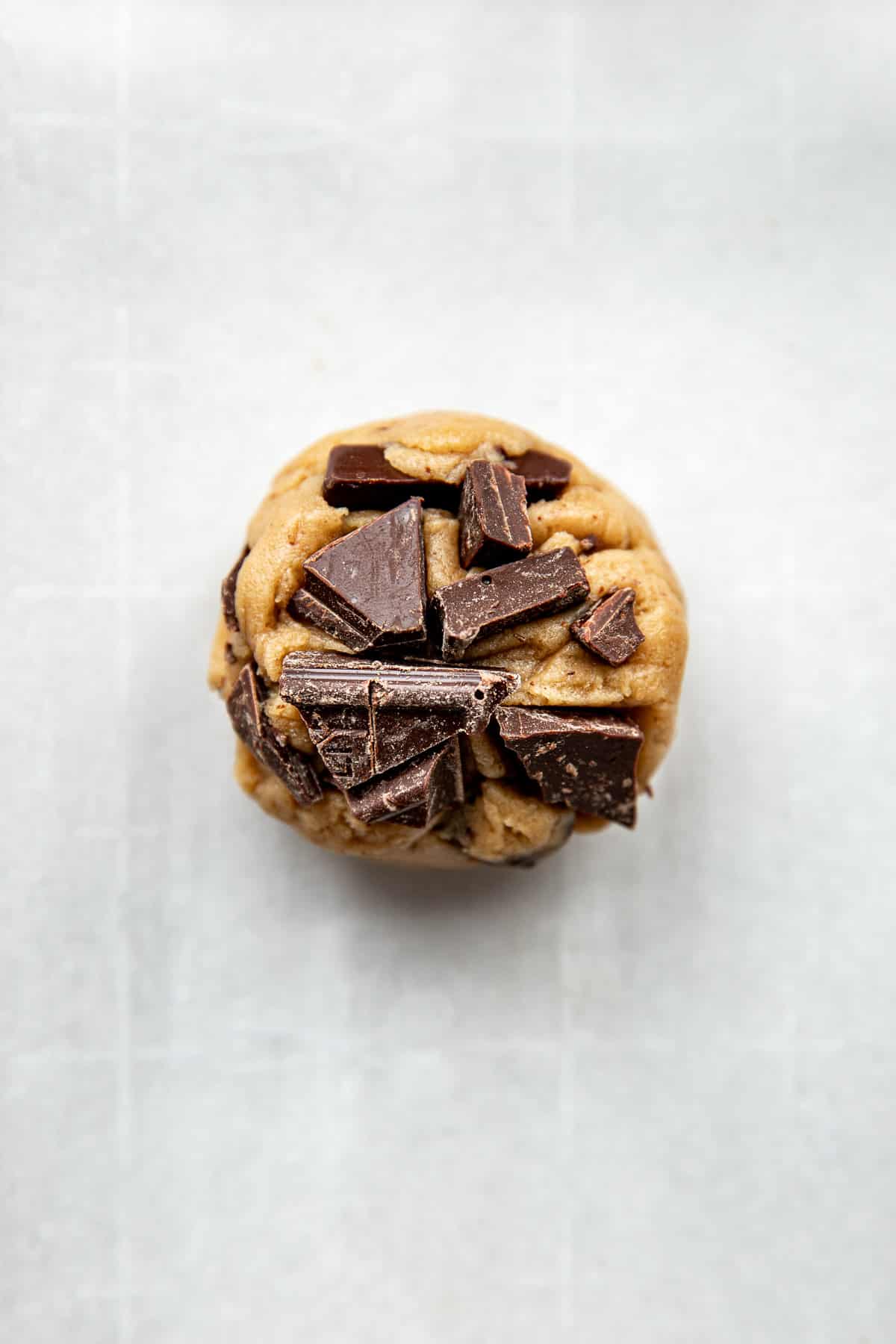 a close up image of a cookie dough ball with chocolate chunks pressed on top. 