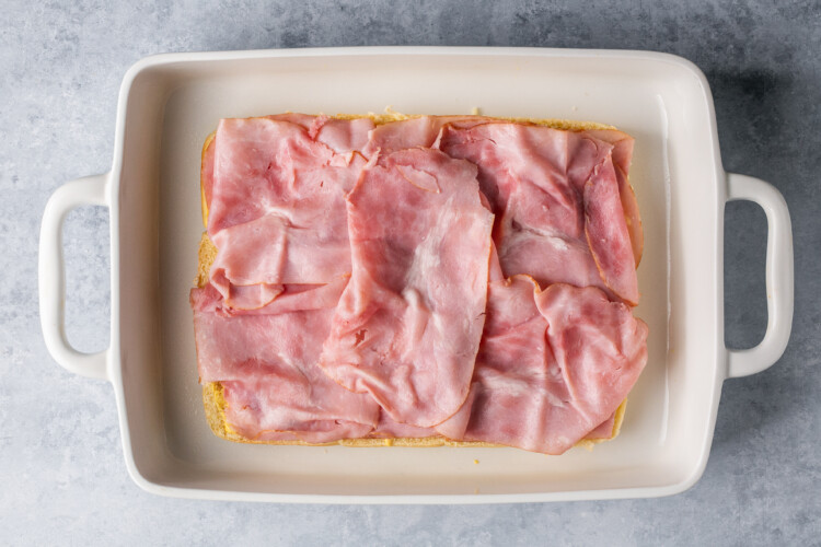 ham slices on dinner rolls in a white baking dish.