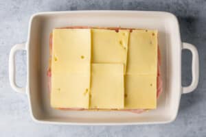 swiss cheese on top of ham on dinner rolls in a white baking dish.