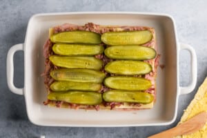 dill pickles on top of pork for cuban sliders in a white baking dish.