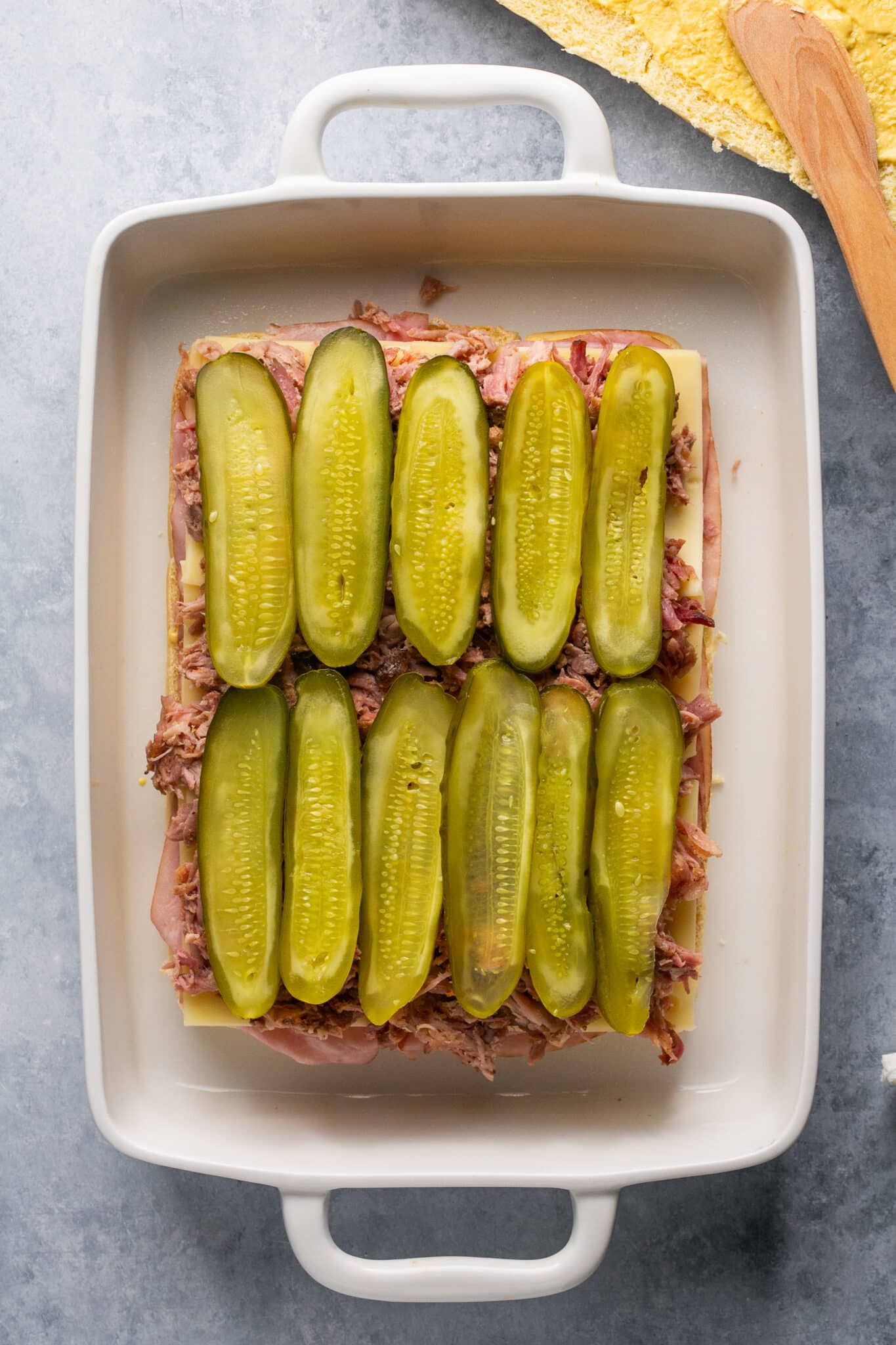 pulled pork and pickles on slider buns in a white baking dish. 